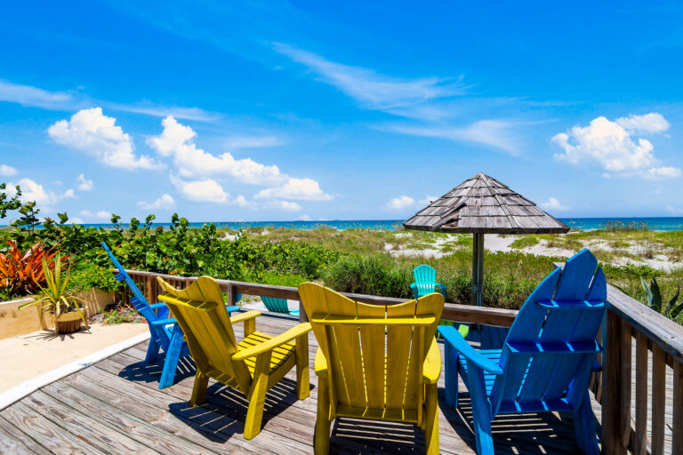 4 beach chairs on a wooden deck facing the ocean with a clear blue sky