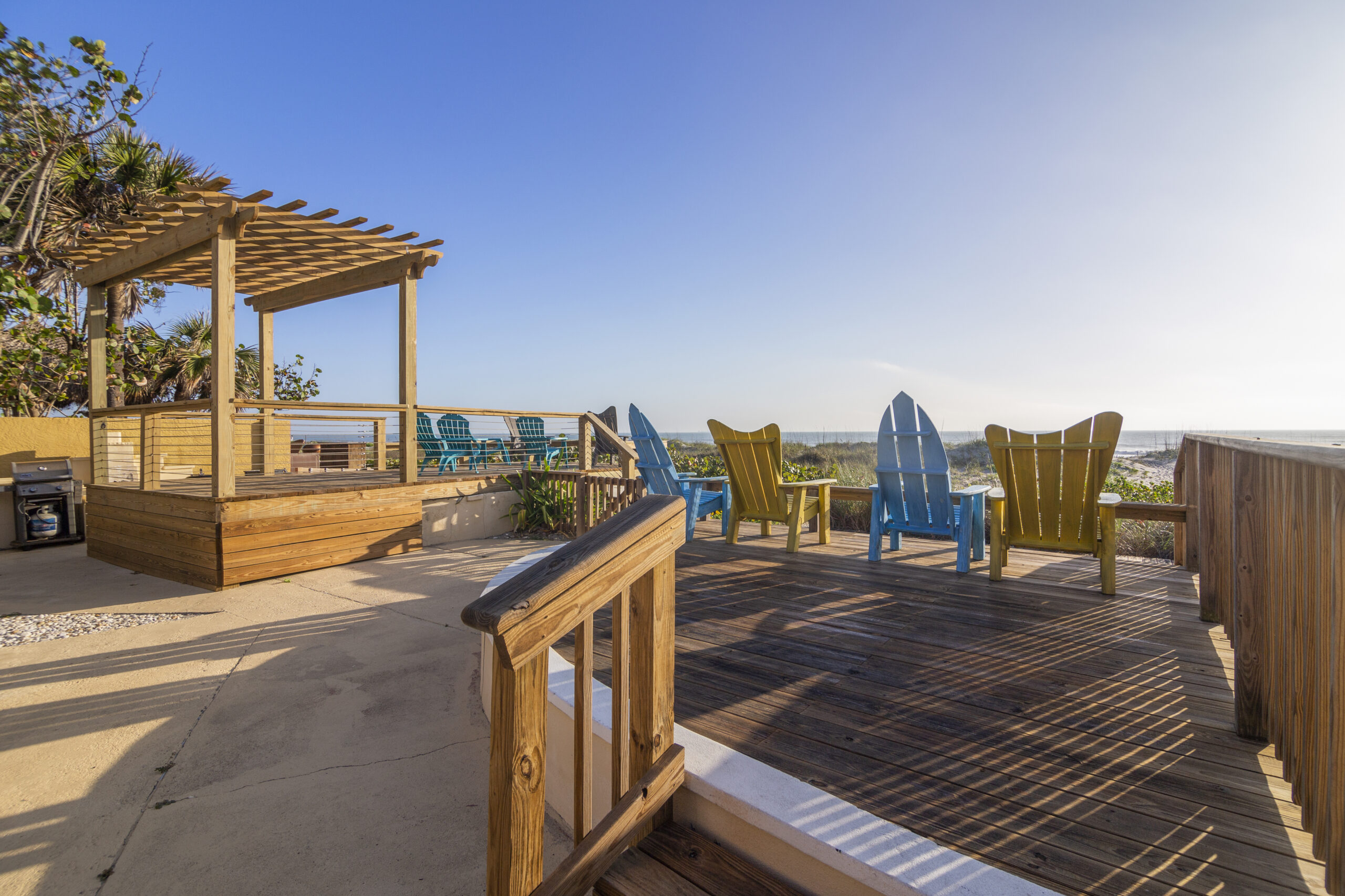 4 beach chairs on a wooden deck facing the ocean with a clear blue sky